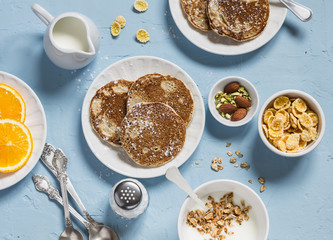 Breakfast table. Whole wheat pancakes, greek yogurt with homemade granola, orange slices, nuts,...