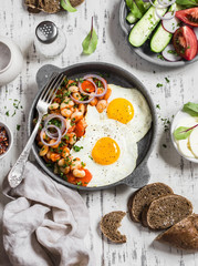 Delicious  breakfast or snack - a fried egg, beans in tomato sauce with onions and carrots, fresh cucumbers and tomatoes, homemade rye bread on light wooden background