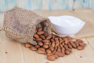 Almonds in brown bowl on textured wooden background
