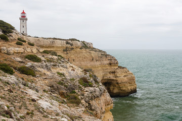 Fototapeta na wymiar Coastal view along the Seven Hanging Valleys Trail with Farol de Alfanzina lighthouse in background, Algarve region, Portugal
