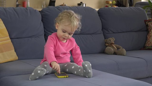 Babysitter help cute baby girl to use smart phone sitting on sofa.