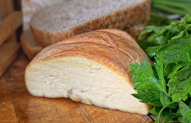 Piece of cheese, bread and greens on a wooden table.