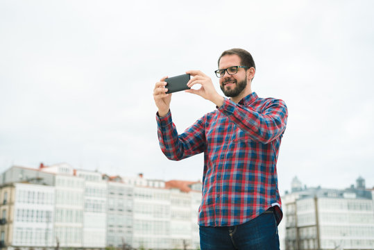Young bearded man taking a picture with his phone outdoors