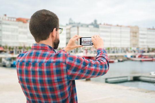 Young bearded man taking a picture with his phone outdoors at a pleasure harbour