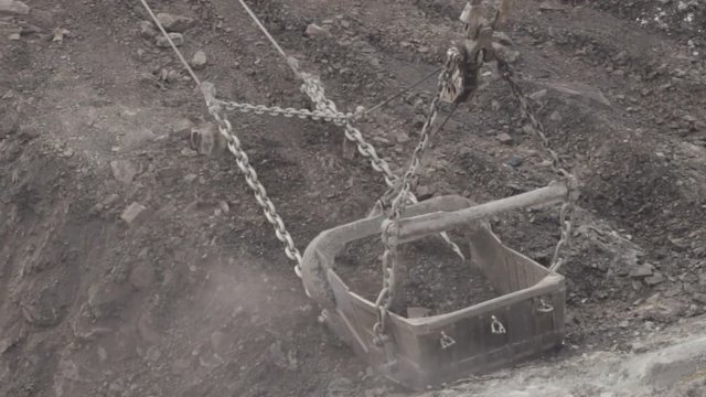 Bucket of a dragline digging grey ground and throws it, closeup.