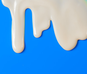 Dripping white milk, cream, paint yogurt on blue background