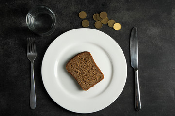 a glass of drinking water and a plate with a slice of bread near cents and Cutlery on a black background.The concept of poverty