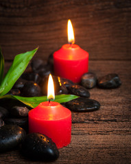 Red candle and black stones on wood background