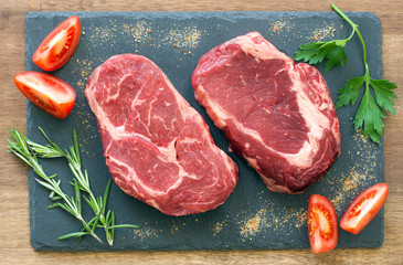 Raw beef steaks with ingredients on a black stone top view