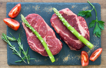 Raw beef steaks with ingredients on a black stone top view
