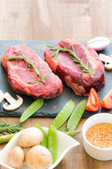 Raw beef steaks with ingredients on a black stone top view