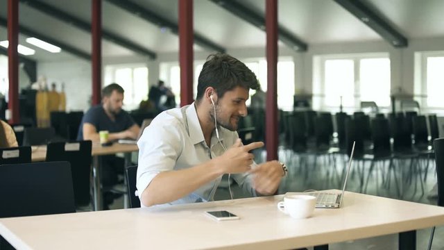 Young entrepreneur with headphones having on-line meeting using notebook during coffee break in office