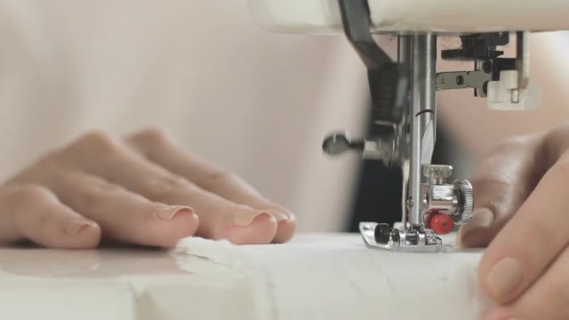 Female hands sewing white fabric on sewing machine