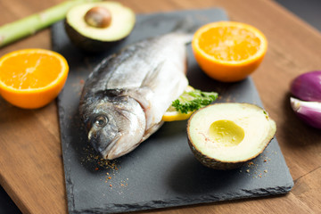 two raw dorado fish with lemon, spices and spoon on paper, composing on white wooden background, top view
