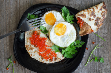 Scrambled eggs and pancakes with caviar on a black plate