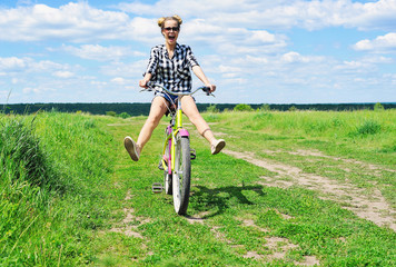 Beautiful girl riding bicycle outdoors across the green sunny field