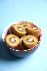 Slices of kiwi fruit on bowl on blue background viewed from abov