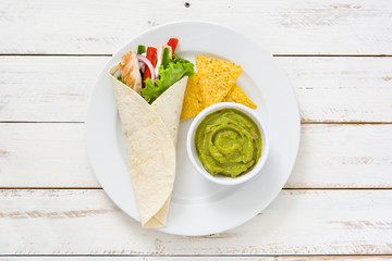 Mexican chicken fajitas with peppers lettuce and onion on a plate and white wooden background

