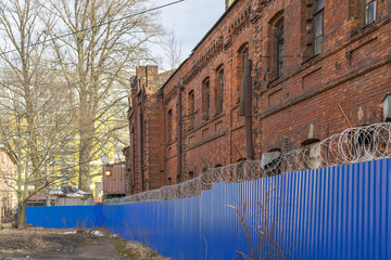The old brick building behind a fence topped with barbed wire