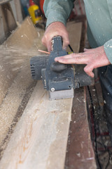 men planing a plank of wood with a electric plane