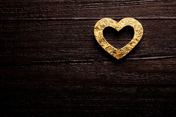 Golden heart over dark-brown wooden background