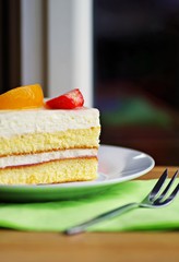 White cream cake with fruity. Fruits cake with cream and jogurt in white plate and fork on a wooden table. Tasty fruit cake desserts.