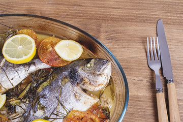 Baked fish with carrot,lemon and greenery.From above