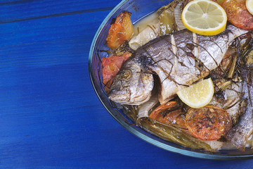 Baked fish with carrot,lemon and greenery.From above