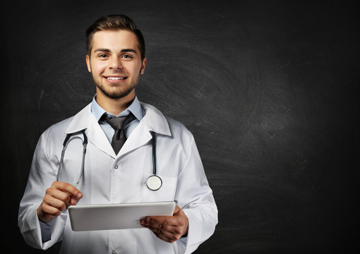 Male doctor with tablet on blackboard background