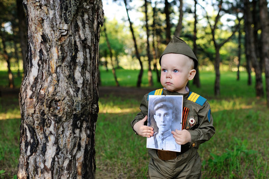 a child in a military uniform of the Soviet army keeps a portrai