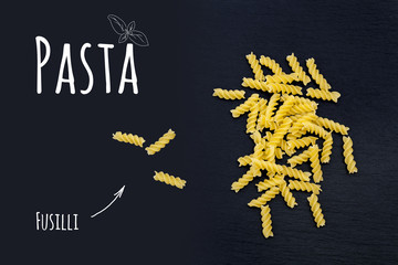 Uncooked Italian pasta Fusilli on black slate stone background with white lettering, top view