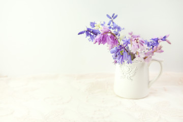 Styled stock floral image, bluebells in a white china jug, on cream lace fabric. Copy space to the left  to overlay your business headline, Facebook or instagram message or other text.
