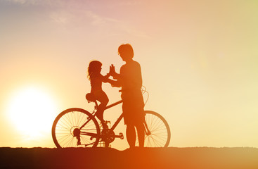 Obraz premium Silhouette of father and little daughter biking at sunset