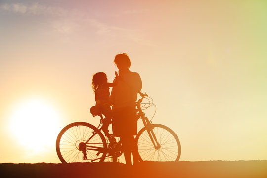Silhouette of father and little daughter biking at sunset