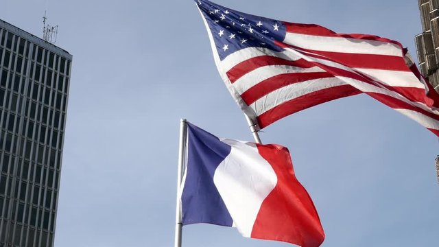 Sun and ray of light behind the waving national flag of United state of America and France with a cloudy blue sky in background