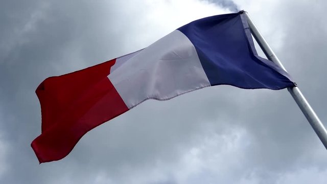 National flag of France waving in the wind with a dark cloudy sky in background