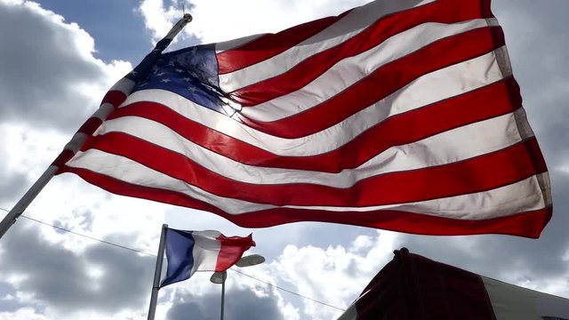 Sun and ray of light behind the waving national flag of United state of America and France with a cloudy blue sky in background