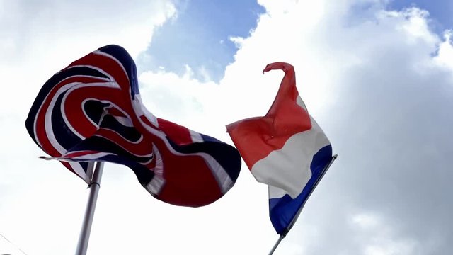 National flag of France and United Kingdom Great Britain England together waving in wind with a cloudy blue sky in background