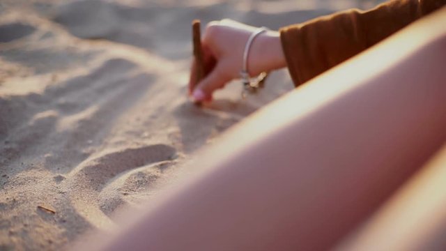beauty girl draws a heart on the sand on sunset beach