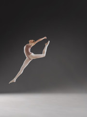 Beautiful ballerina posing in jump on gray background