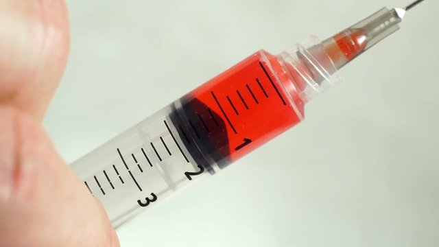 Close up macro shot of a red liquid in a hypodermic needle syringe for medical and health care injections being squeezed.