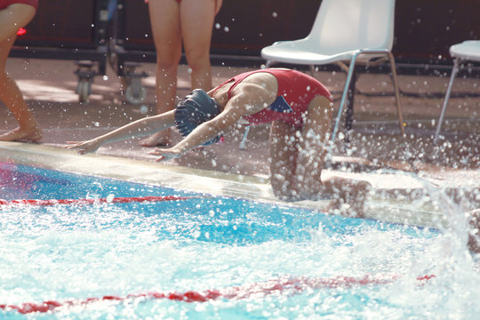 Red swimming suit girl with black swimming cap jumping at the pool side