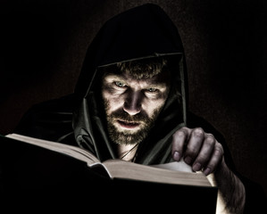 necromancer casts spells from thick ancient book by candlelight on a dark background