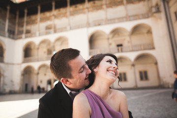 Beautiful couple, man, girl with long pink dress posing in old castle near columns. Krakow Vavel