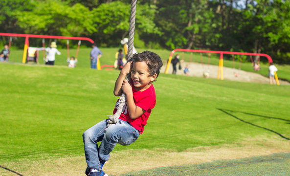 Smiling Asian boy swinging on a rope at a playground