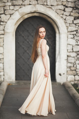 Naklejka premium Young woman with long dress and hair posing in park near old gate