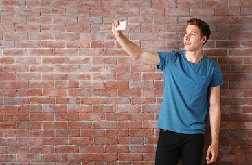 Fototapeta na wymiar Young handsome man taking selfie on brick wall background