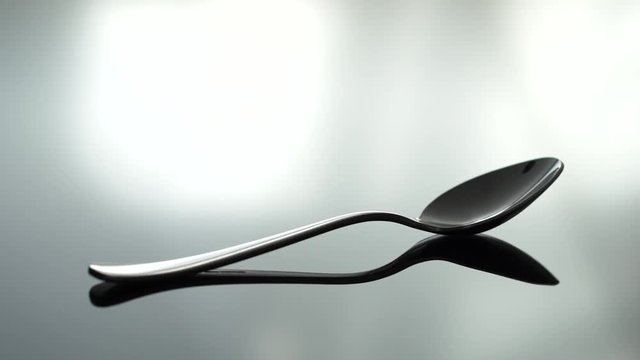 A tea spoon beeng placed on a reflecting table, shallow focus