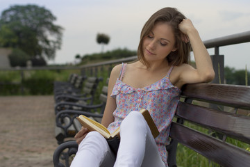 Young girl on the bench reading a book in natural background