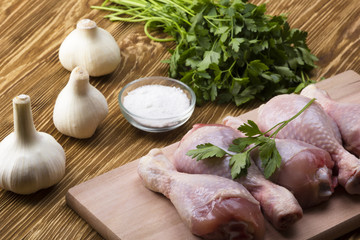 raw chicken drumstick on the board with salt, garlic, parsley
